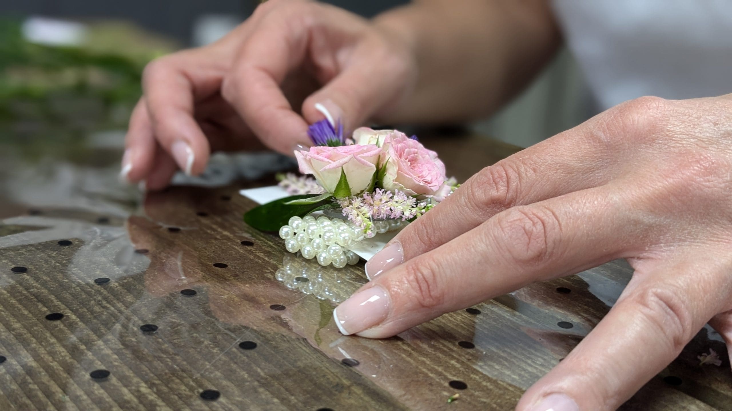 Florists hands carefully arranging a small set of pink flowers and pearls