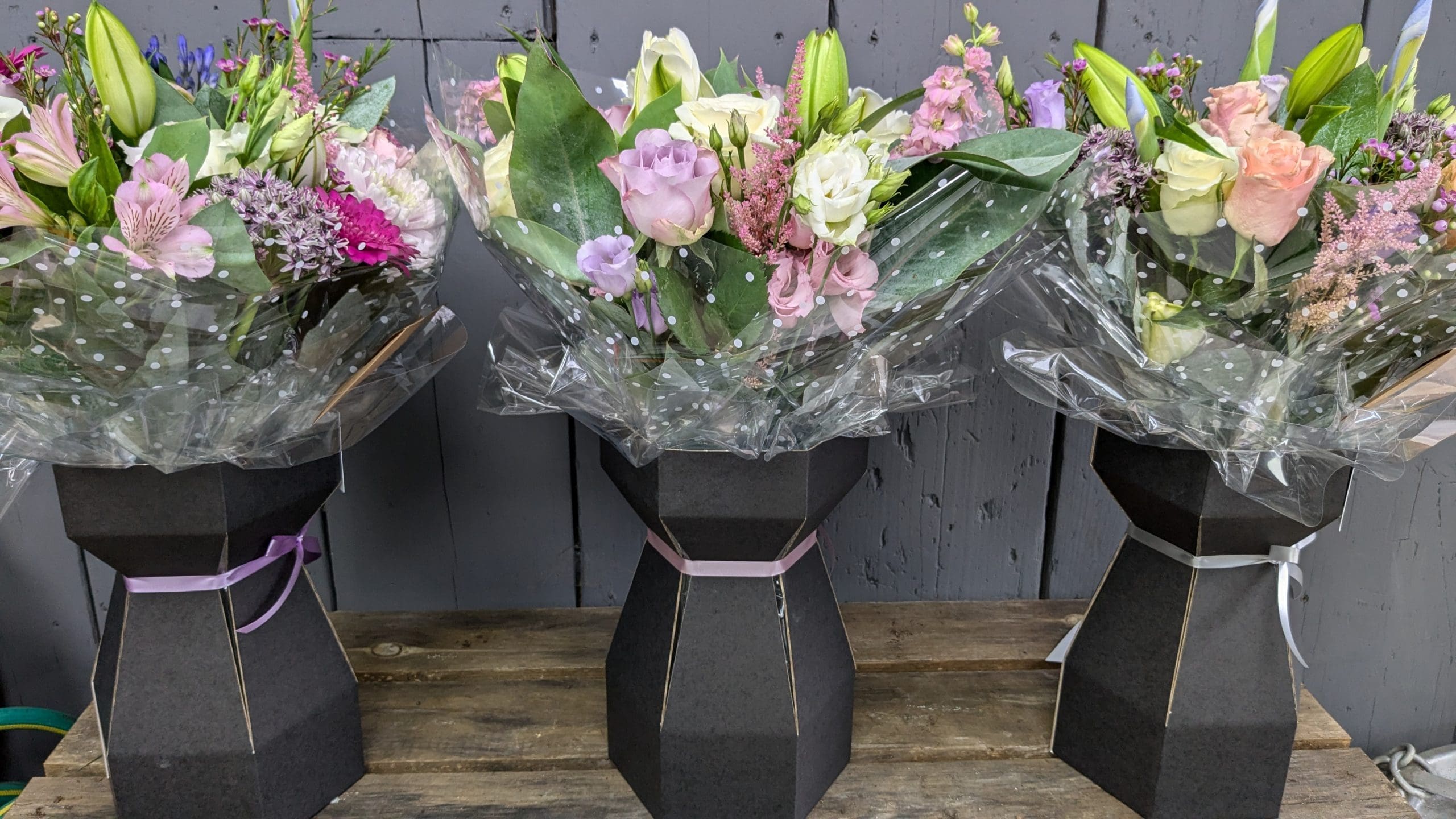 Set of 3 florist choice bouquet of flowers on a wooden display in the garden of eden flower shop